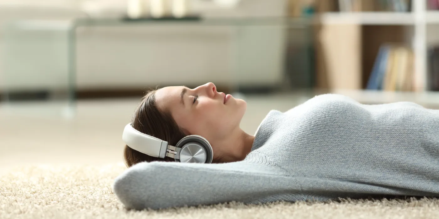 Frau liegt entspannt mit Kopfhörern zu Hause und hört ein Audio-Hypnose-Programm – die Bestseller von Dr. Eisfeld bequem als Sofort-Download